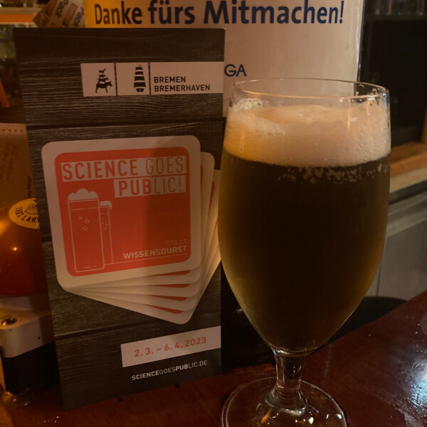 Vor dem Flyer von "Science goes Public" steht ein gefülltes Bierglas auf dem Tisch.